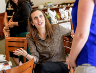 A woman sits on a chair and speaks with a colleague - Pepperdine University